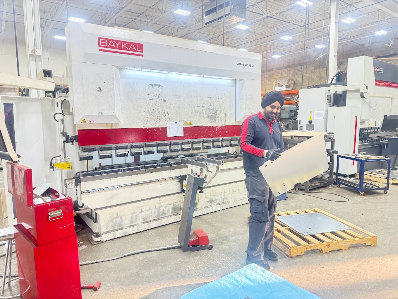 Operator inspecting bent sheet metal part at Baykal APHS-31160 CNC press brake