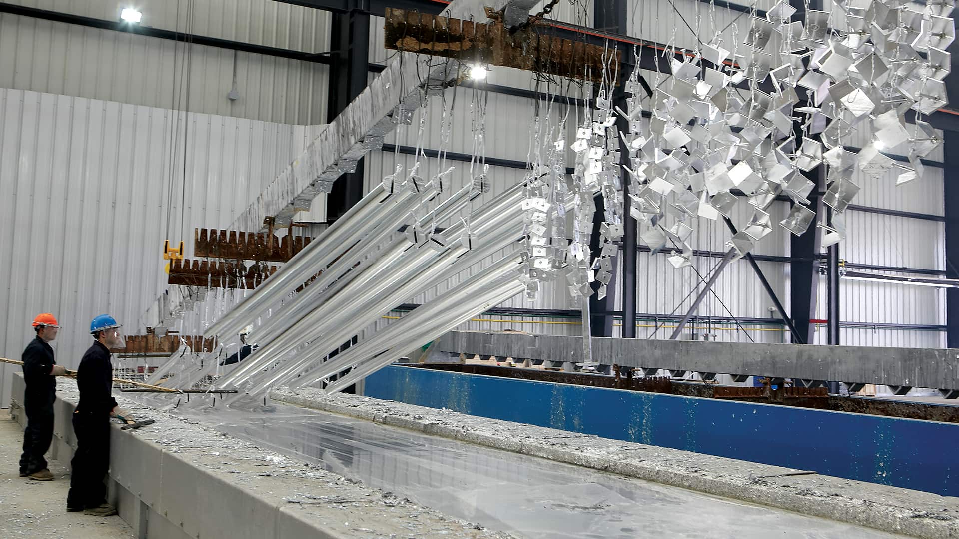 Galvanizing line with suspended fabricated metal parts moving through a zinc bath.