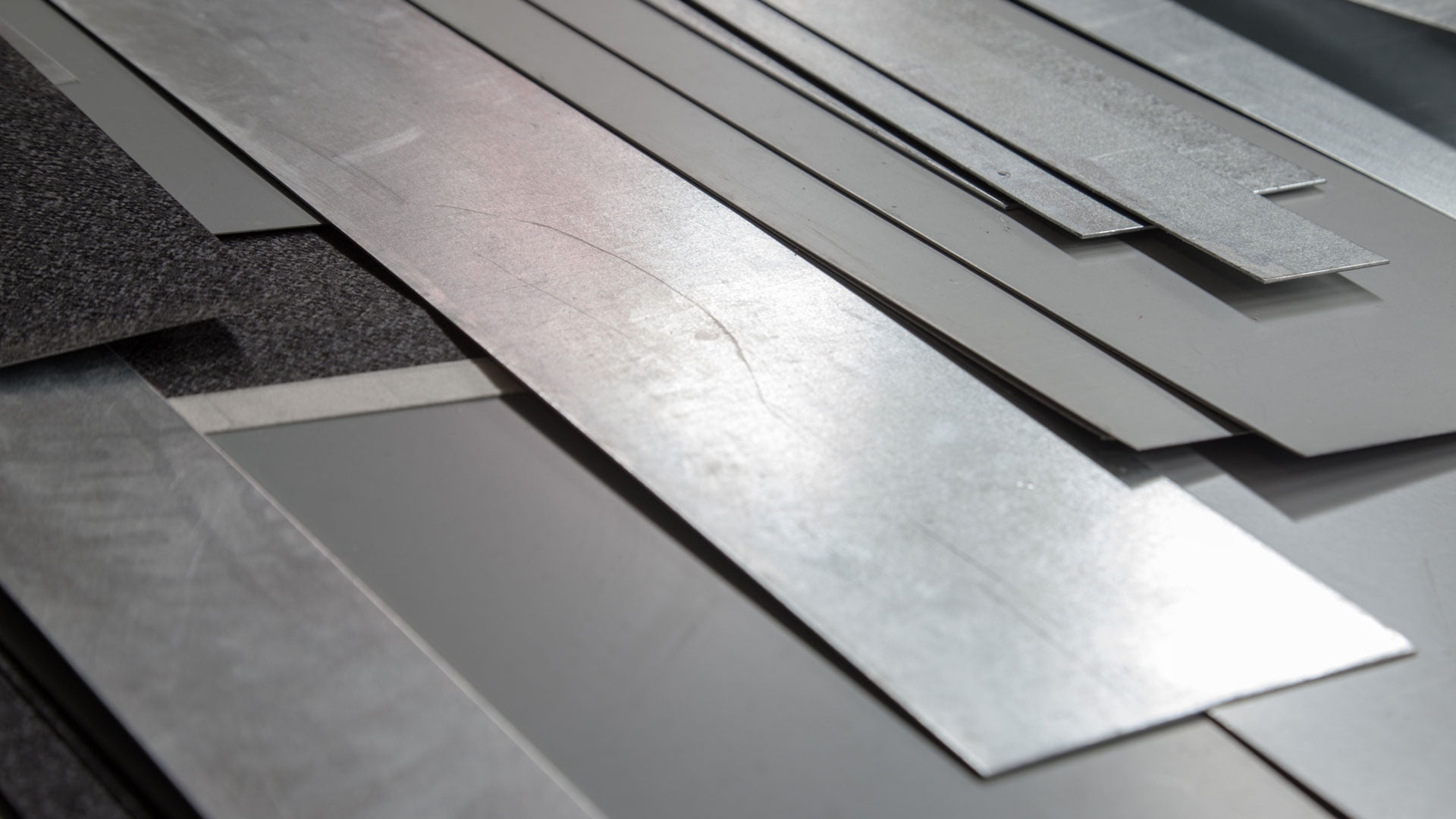 Sheet metal samples laid out on a bench to compare material thickness and finish.